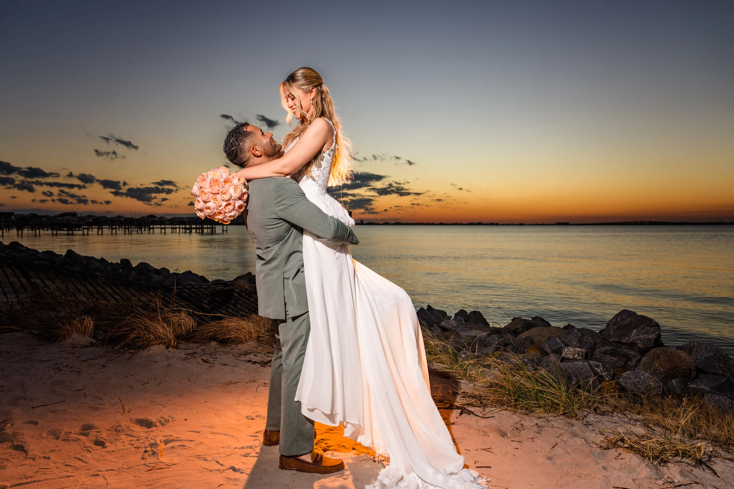 A bride and groom embracing beside the bay at sunset